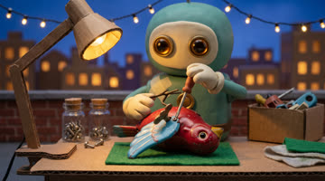 Bo, a clay robot, tightens a tiny screw on a red tin bird's wing under a desk lamp